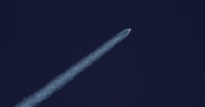 A rocket ascends into the sky, leaving a trail of smoke against the clear blue sky.