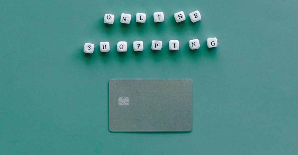 Flat lay of credit card and 'Online Shopping' text on green background, symbolizing ecommerce.