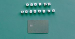 Flat lay of credit card and 'Online Shopping' text on green background, symbolizing ecommerce.